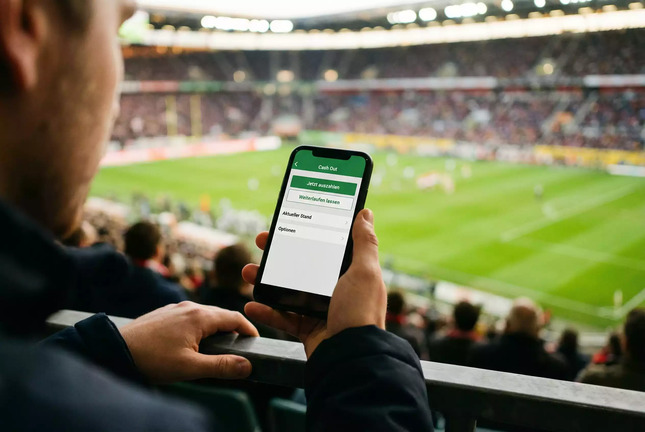 Hand eines Zuschauers hält ein Smartphone mit Wettapp während eines NFL-Spiels im Stadion