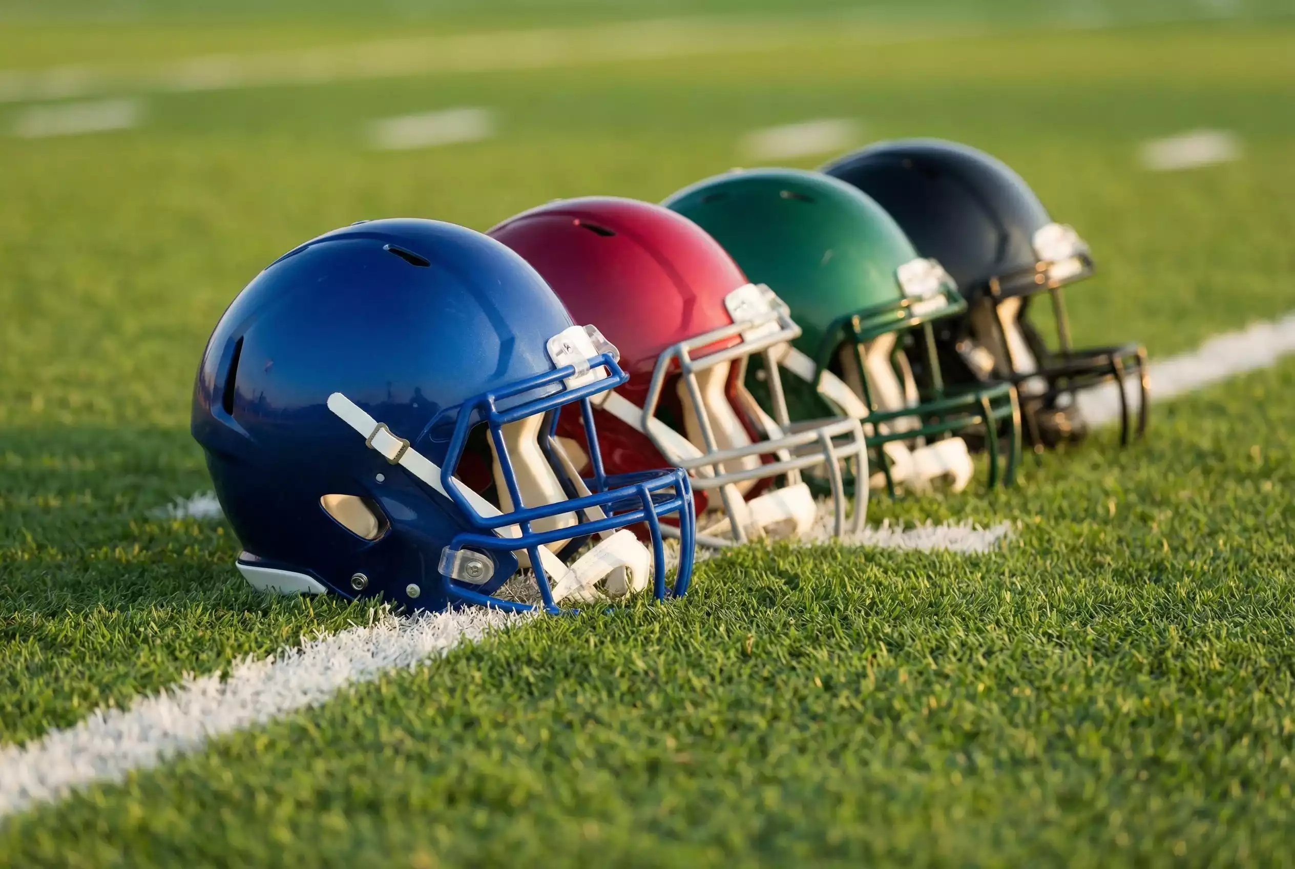 Vier American Football Helme in verschiedenen Farben nebeneinander auf dem Rasen