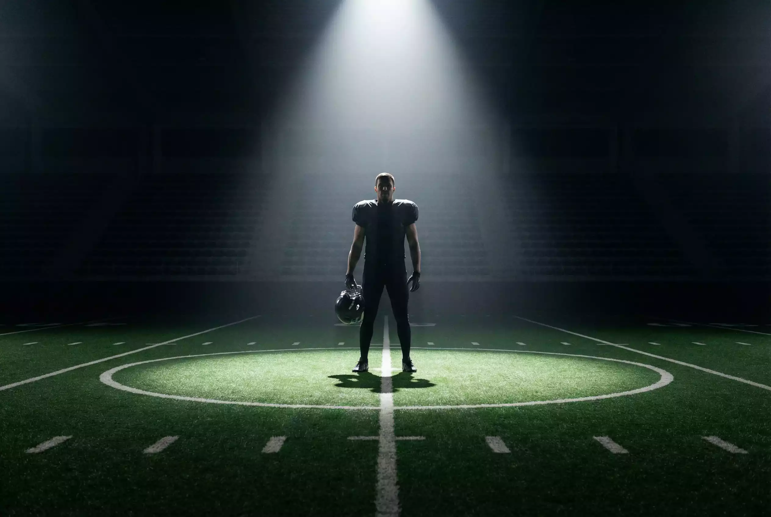 American Football Spieler steht allein im Scheinwerferlicht auf dem Spielfeld