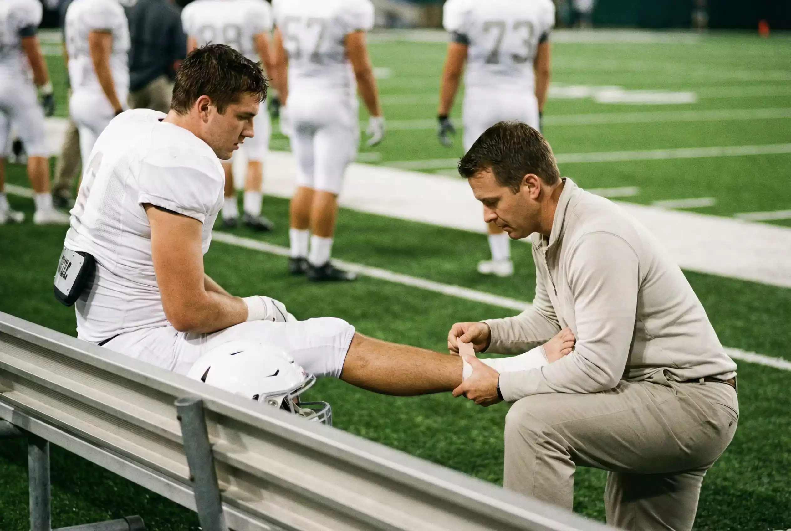 American Football Spieler sitzt auf der Seitenbank und wird vom Teamarzt untersucht