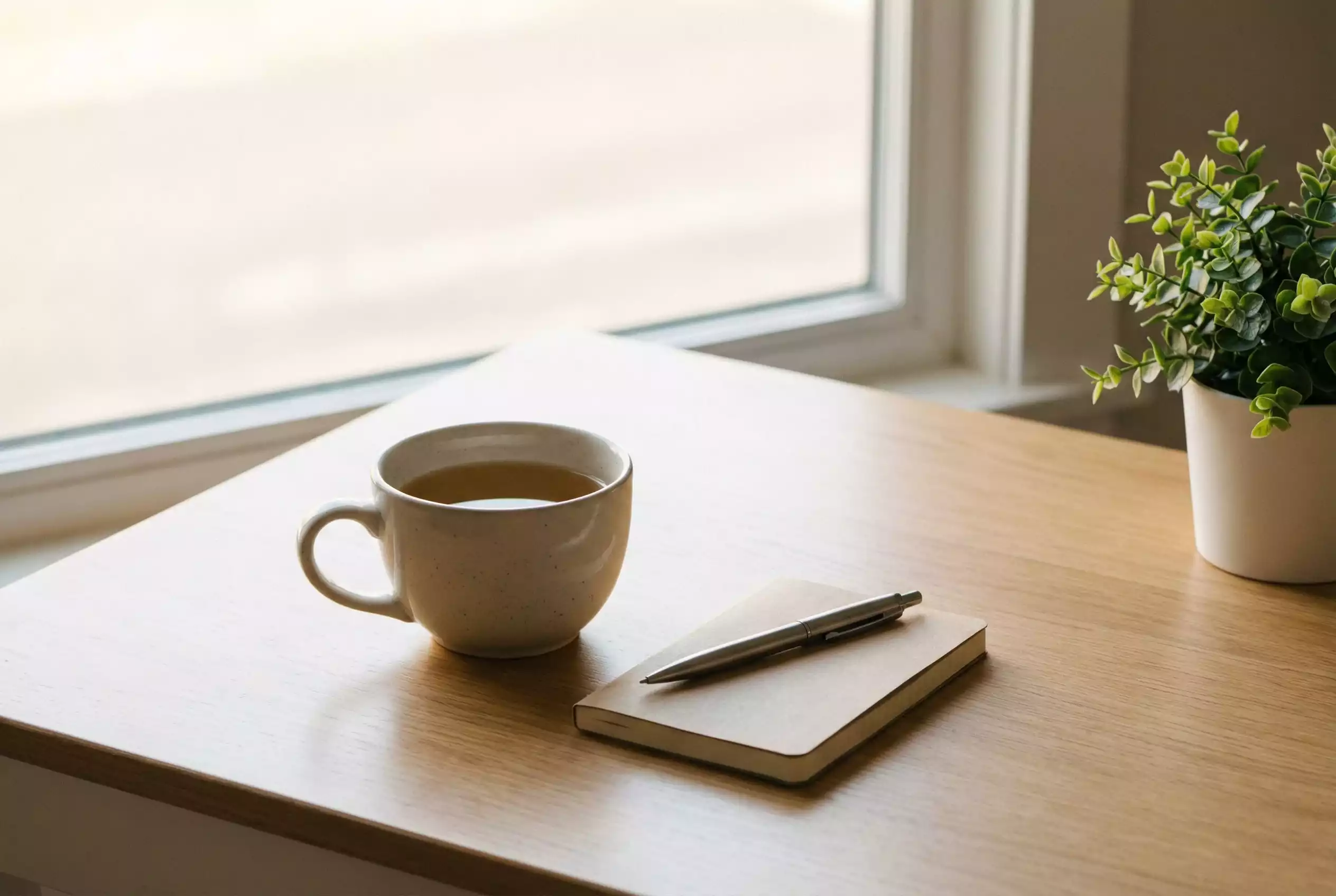 Ruhige Szene mit einer Tasse Tee und einem Notizbuch auf einem Holztisch bei warmem Licht